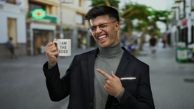 Young man outdoors in city street holding 'i am the boss' mug with a confident smile, showcasing modern urban lifestyle and casual attitude in dynamic urban environment.