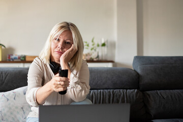 Mature woman feeling bored watching television while working from home