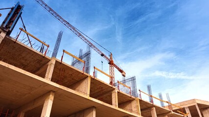 Construction of a multi-storied building with metal armature on the top. Yellow crane towers above the structure. Low angle view.