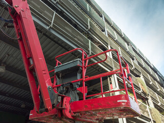 Red aerial work platform extending upwards for maintenance work on a modern building