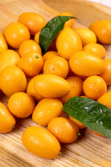 Fresh kumquats on wooden board with green leaves