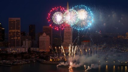 Fireworks burst above a cityscape at night, illuminating the sky with vibrant colors and patterns. The city skyline is silhouetted against the dark sky. Stock Video