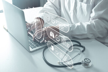 Doctor working on laptop with holographic medical icons and stethoscope, representing telemedicine, digital health, AI diagnosis, and future healthcare technology concept on white desk.