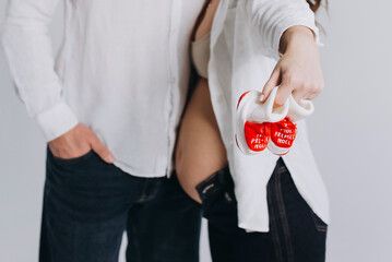 Pregnant couple holding baby booties that say 'My First Christmas,' symbolizing holiday anticipation and joy.