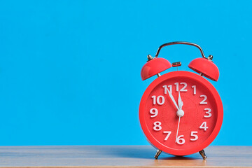 Red alarm clock on wooden table and blue background with copy space.