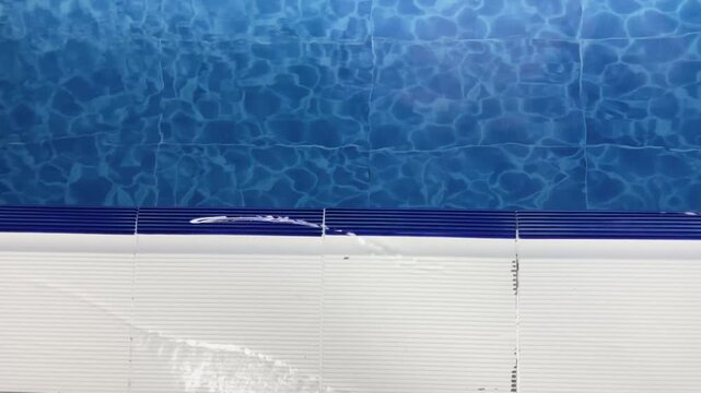 Blue pool water at the edge, water flowing from the overflow grate and reflections of light. Ideal for cleanliness, summer, sports, or water-themed content, offering a modern and clean look.
