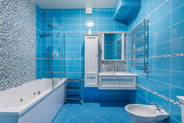 A bathroom with blue tiles features a tub and a separate shower area. A mirror hangs above the sink...