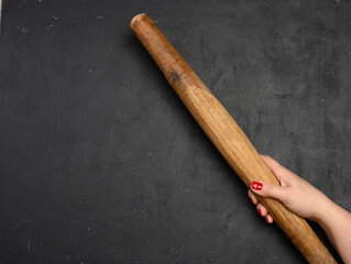 Female hand holding a vertical antique wooden rolling pin against a black background.