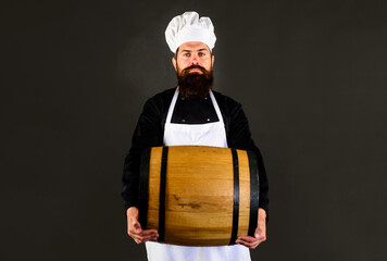 Brewer in apron holds barrel with craft beer. Serious man carrying wooden barrel with wine. Winemaking. Handsome male chef with oak barrel or cask of beer for pub or bar. Bearded man with beer barrel.