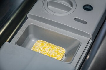 Dishwasher detergent tablet in machine dispenser tray. Household kitchen appliance cleaning and hygiene concept for home wash cycle.