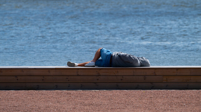 Relaxing person resting on wooden platform beside waterfront on sunny day. - Powered by Adobe