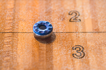 Blue shuffleboard puck on polished wooden scoring lane.