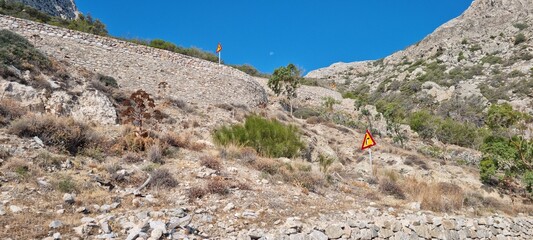 Danger sign on a winding mountain road in a rocky landscape under a clear blue sky