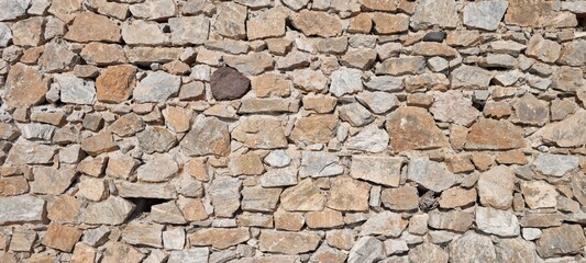 Natural stones form wall structure with various sizes and colors in outdoor setting during daylight