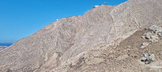 Mountain slope in a clear sky with a distant lighthouse visible on top during daylight hours