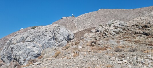 High rocky terrain with clear blue sky in the background and distant structures on the mountain top during a sunny day