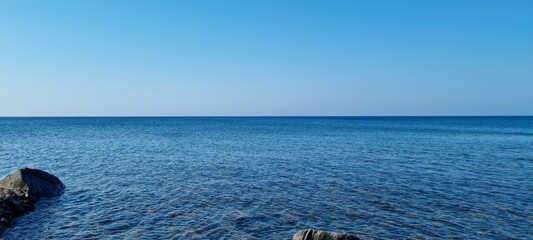 Bright blue ocean meets clear sky on a sunny day in coastal area with rocks along the shore