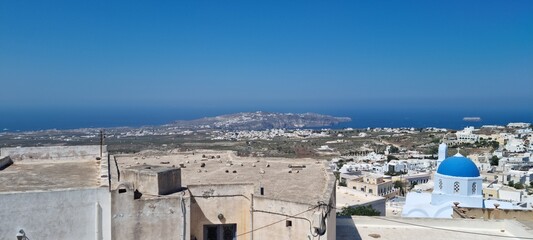 View of Santorini island from high vantage point showing buildings and blue dome under clear sky