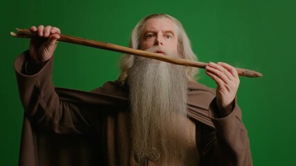 An old man, dressed in traditional robes, holds a wooden staff against a green screen background, exuding an aura of mystery. Stock Video