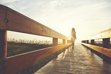 Obraz premium Woman, bridge or boardwalk at beach with sunset, happy with below space and vacation for summer travel. Adventure, portrait or person in bikini for coastal holiday, sunshine and walk on wood pathway