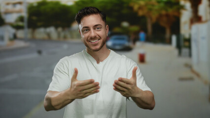 Young man with beard smiles outdoors on city street, expressing joy and open arms in urban...