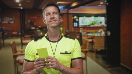 Referee man holds yellow card and whistle in a restaurant building interior with hands gripping card; authority.