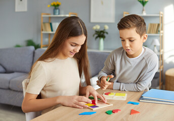 Developmental activities at home. Two children are assembling colorful wooden puzzle pieces and playing logic games at home. Girl and boy are making various geometric shapes while sitting at table.