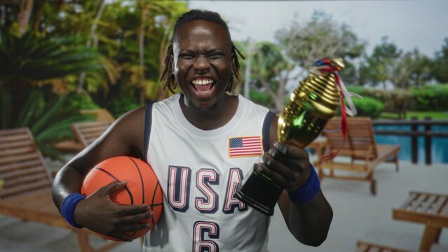 Man holding basketball and gold trophy, hand gripping ball, shouting in building poolside resort; victory celebration pride.