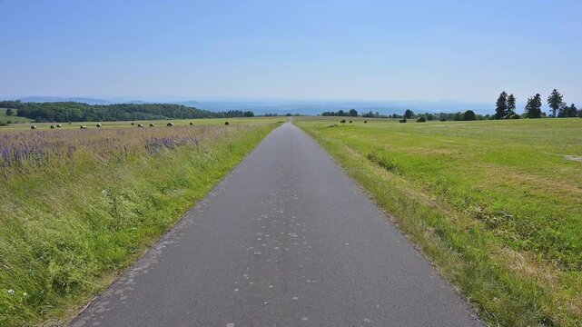 Strasse durch eine weitl&auml;ufige Landschaft mit gr&uuml;nen Wiesen und entfernten H&uuml;geln unter blauem Himmel, Koppelhutweg, Lange Rh&ouml;n, Hausen, Rh&ouml;n, Bayern, Deutschland, Europa