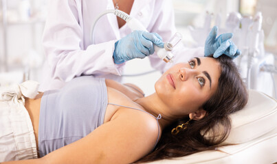 Young brunette undergoing facial procedure with application of atomized nutrients to enhance skin...