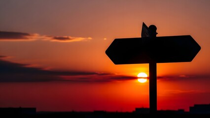 Silhouetted Blank Double-Sided Signpost Standing Against a Dramatic Red and Orange Sunset or Sunrise Sky, Symbolizing Choice and Direction