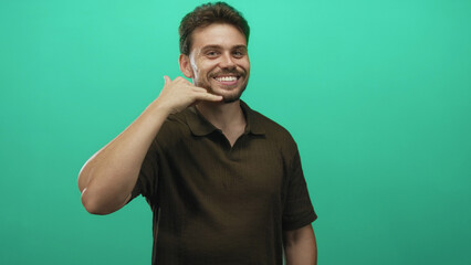 Young hispanic man pointing at camera and making call gesture, smiling in studio with green...