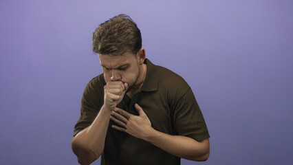 Young hispanic man coughing into his fist with one hand pressed to his chest in a purple studio...