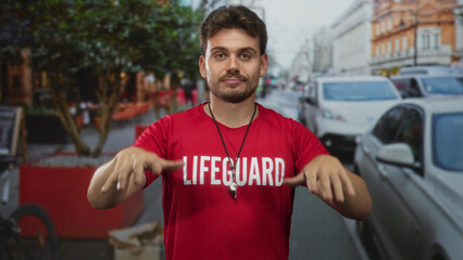 Man lifeguard in red shirt with whistle and hands extended reaching forward on street; duty...