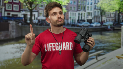 Young hispanic man lifeguard holding binoculars and whistle, showing thumb down gesture on street...