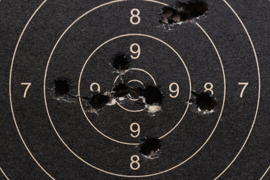 Close-up of a well-used black and white paper shooting target riddled with bullet holes, showing precision grouping in competitive marksmanship.