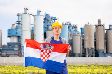 Sad woman in overalls with Croatia flag in her hands against the background of chimneys of a modern...