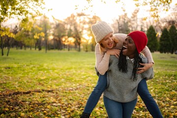 Fototapeta premium Diverse friends piggybacking giggling together in autumn park