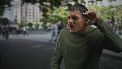 Fototapeta premium Man with visible face and right hand lifted near ear standing center frame among blurred pedestrians and buildings on street; pensive solitude.