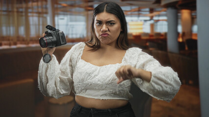 Woman adjusting a dslr camera with her hand, inspecting the lens in an airport lounge near windows and pillars; concentration practice.