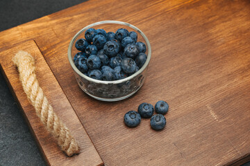 Fresh blueberries in a glass bowl on a wooden tray with some berries placed nearby