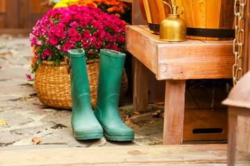Green rubber boots near colorful flowers and wooden bench at a garden setting on a bright day