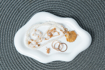 Jewelry arranged on a white dish with a textured gray background during daylight