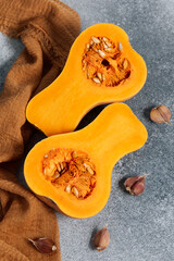 Fresh butternut squash cut in half on gray surface with garlic cloves nearby