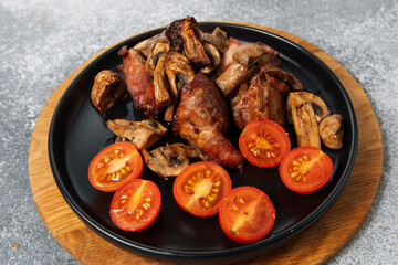 Grilled meat and mushrooms with sliced tomatoes on a round black plate