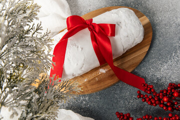 Baked dessert with red ribbon placed on wooden board near winter decorations and berries