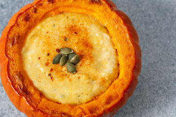 Fresh pumpkin filled with pumpkin cream soup and topped with seeds on a gray surface during autumn season