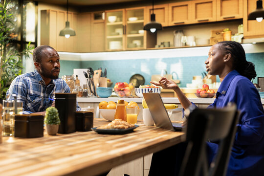 Happy black couple creating a grocery list to compare products and order food, shopping online using a laptop in their kitchen for products and perishable items. Healthy lifestyle and e-commerce.