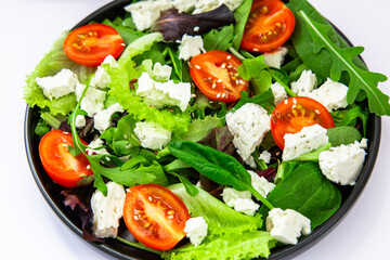 Fresh salad with lettuce cherry tomatoes and cheese on a black plate in a kitchen setting