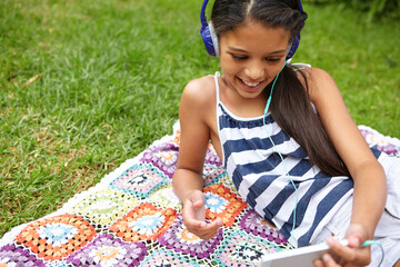 Happy girl, listening and music with headphones on picnic blanket for audio streaming in nature. Child, teenager or kid with smile or phone for sound playlist or entertainment on grass field in park